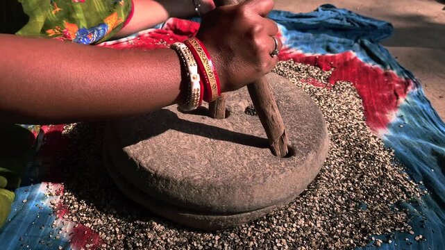 A close-up view of an Indian woman working with a stone quern to grind urad dal highlights traditional village life, sustainable living, and authentic culinary heritage.