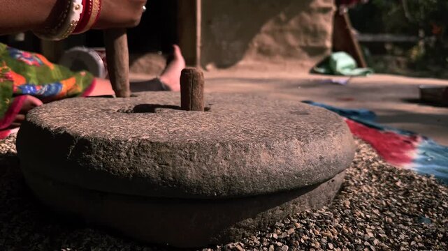 An Indian village woman grinding black gram lentils on a hand-driven stone mill showcases traditional agriculture-based lifestyles, homemade food culture, and timeless rural craftsmanship.