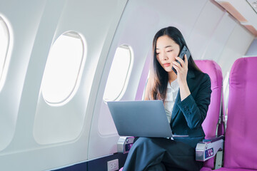  A woman is sitting on an airplane, working and looking at her laptop.