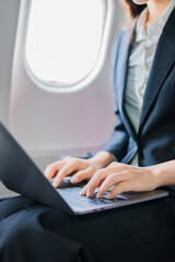  A woman is sitting on an airplane, working and looking at her laptop.