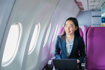  A woman is sitting on an airplane, working and looking at her laptop.