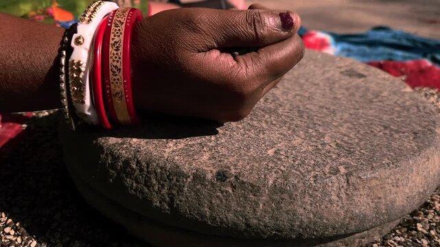 Indian woman in a rural setting using a traditional hand-operated millstone, also known as a quern, to grind Black gram lentils.
