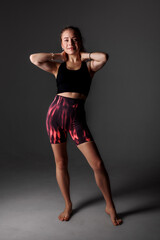Fototapeta premium Young woman poses confidently in athletic wear against a dark background during a fitness photo shoot