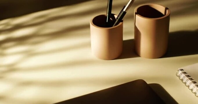 Desk with art supplies and notebook bathed in warm sunlight and shadows.