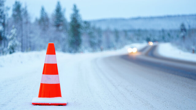 Traffic cone on snowy rural road in poor visibility, dangerous icy conditions in winter landscape, road warning in low contrast weather, accident risk alert, frozen route safety emergency situation