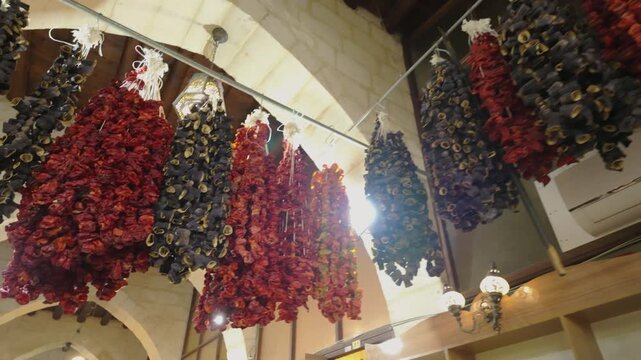 Cinematic 10-bit slow motion showing colorful strings of dried bell peppers and eggplants hanging from the ceiling of a historical inn (han) in Turkey. Traditional food preservation methods.