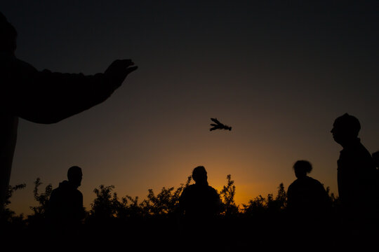 Silhouettes of five men playing a traditional Chinese shuttlecock kicking game outdoors at sunset.