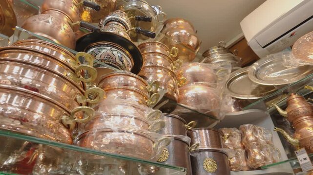 Close-up 10-bit slow motion of various handmade copper pots, pans, and teapots displayed on glass shelves in a traditional Turkish shop. Showcasing authentic metal craftsmanship. 4K quality.