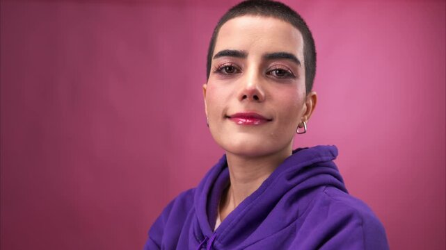 Portrait of young woman cheerful young woman with a buzz cut smiling confidently against a pink background