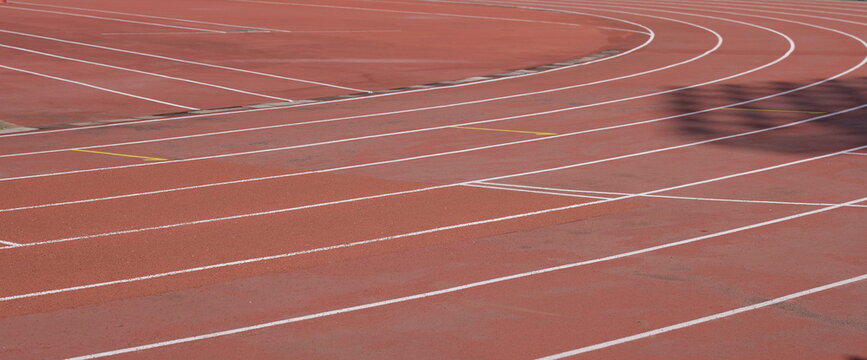 Empty red running track with white lane markings curving through the frame