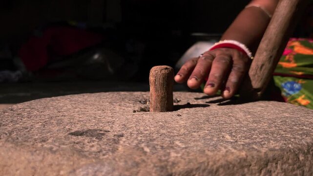 A close-up view of an Indian woman working with a stone quern to grind urad dal highlights traditional village life, sustainable living, and authentic culinary heritage.