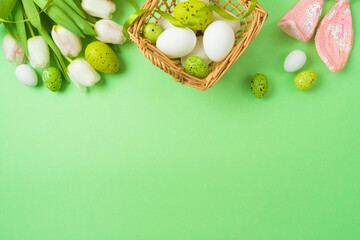 Easter holiday concept with easter eggs, basket and white tulip flowers on green background. Top view, flat lay