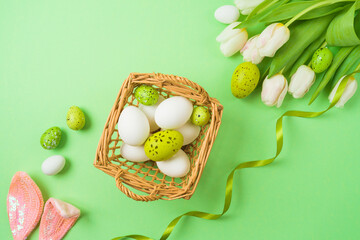Easter holiday concept with easter eggs, basket and white tulip flowers on green background. Top view, flat lay