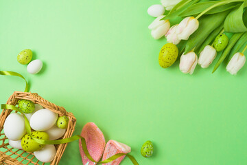 Easter holiday concept with easter eggs, basket and white tulip flowers on green background. Top view, flat lay