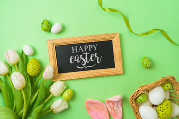 Easter holiday greeting card with chalkboard, easter eggs, basket and white tulip flowers on green background. Top view, flat lay