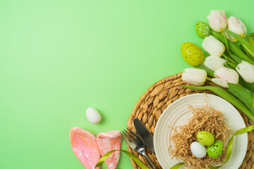 Easter festive table setting with easter eggs decoration and white tulips flowers on green background. Top view , flat lay