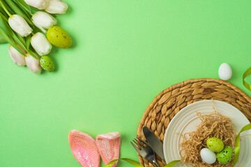 Easter festive table setting with easter eggs decoration and white tulips flowers on green background. Top view , flat lay