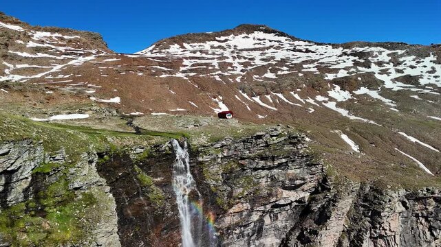 Aerial drone view of the mountain shelter Bivacco Piano della Parete in Switzerland. Surrounded by mountains and a waterfall, silence and serenity prevail. Outdoor adventure and a traveling lifestyle.