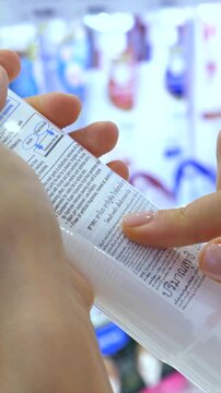 Close up of a female customer carefully reading the label and ingredients on a cosmetic cream tube while shopping for skincare products in a retail store or pharmacy