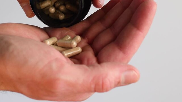 Close up man hand pouring capsules from bottle into palm; taking medicine or supplements for healthcare. Medication treatment daily routine wellness. Brown pills nutritional supplement pharmacy health
