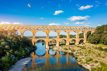 Fototapeta premium Aqueduct of Pont du Gard arches over the river, showcasing the rich history of Vers-Pont-du-Gard, France. Ancient aqueduct of Pont du Gard spans the peaceful river in Vers-Pont-du-Gard, France.
