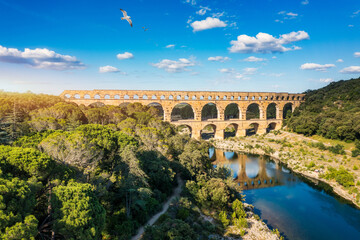 Naklejka premium Aqueduct of Pont du Gard arches over the river, showcasing the rich history of Vers-Pont-du-Gard, France. Ancient aqueduct of Pont du Gard spans the peaceful river in Vers-Pont-du-Gard, France.