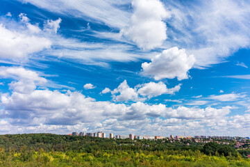 View of Prague city skyline is visible, creating a beautiful contrast with nature. Expansive blue sky with fluffy clouds over green landscape and Prague city skyline in the distance. Prague, Czechia.