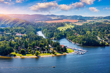 View of Slapy in Czechia showcasing the peaceful lake and surrounding lush greenery on a sunny day. Slapy reveals a tranquil lake surrounded by hills, dotted with boats and greenery. Slapy, Czechia.
