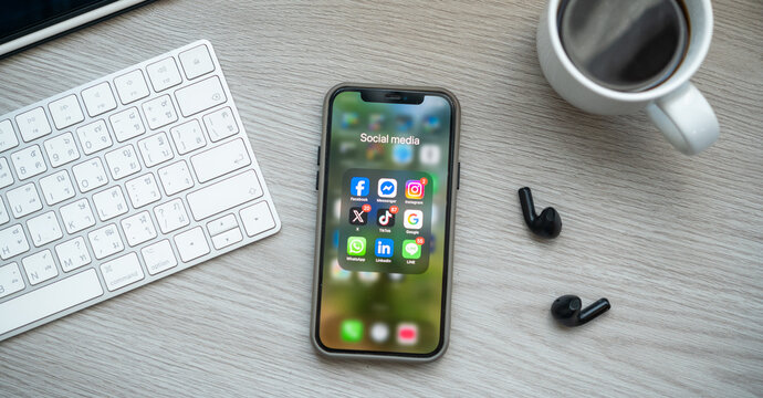 Bangkkok, THAILAND - January 2nd, 2026: Iphone with icons of social media on screen place on table with tablet and ear phone and a mug of coffee