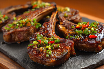 Grilled lamb chops with herbs and spices on wooden cutting board at kitchen setting