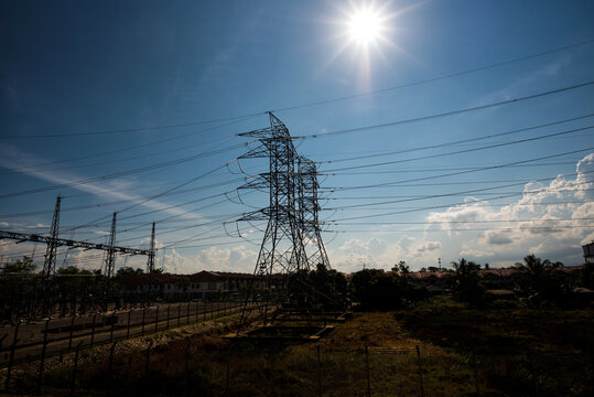 High Voltage Transmission Towers in the Afternoon Sun - Showcases towering high-voltage electricity pylons and power lines stretching across a bright blue sky with the sun shining intensely overhead.