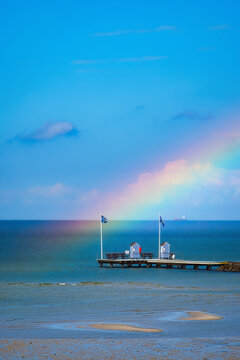 A wooden walkway of a pier on the Baltic Sea with two changing rooms and a rainbow.
