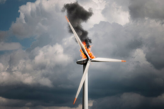 A wind turbine generating electricity, with fire and smoke in front of dark storm clouds.