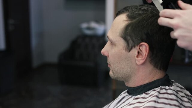 A young male Barber adjusts the hair of a male client. Professional hair care products. Cinematic close-up of a barber giving fade haircut to male client. Slow motion shot of short clipper hairstyle.