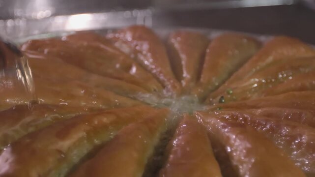A wide-angle, 10-bit slow motion shot of a traditional Gaziantep baklava workshop. Featuring golden trays of thin-layered pastry being finished with hot syrup in a professional kitchen.