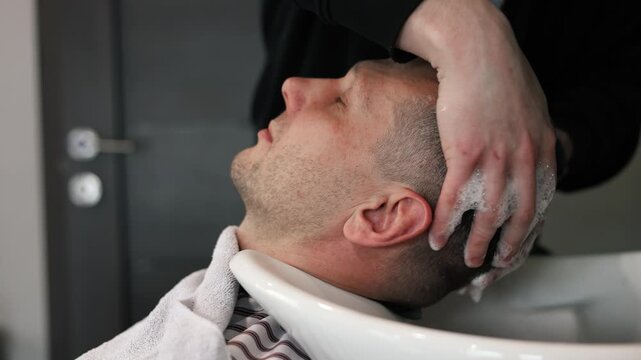 A young male Barber adjusts the hair of a male client. Professional hair care products. Cinematic close-up of a barber giving fade haircut to male client. Slow motion shot of short clipper hairstyle.