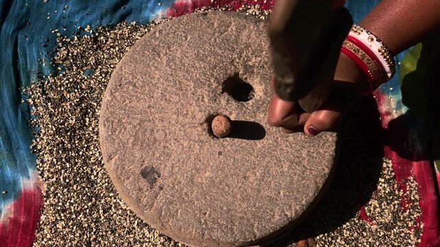 In a rural Indian household, a woman carefully grinds black gram lentils using a traditional hand-operated millstone, preserving age-old food preparation methods passed down through generations.