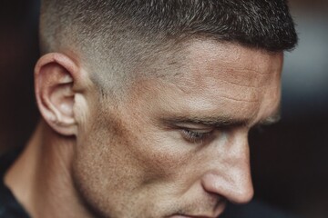 Obraz premium Man looking down, showing a modern faded haircut and a thoughtful expression