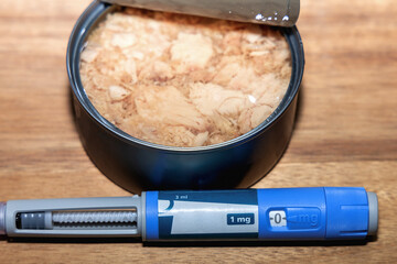 Open tuna can and ozempic injection pen on wooden board.