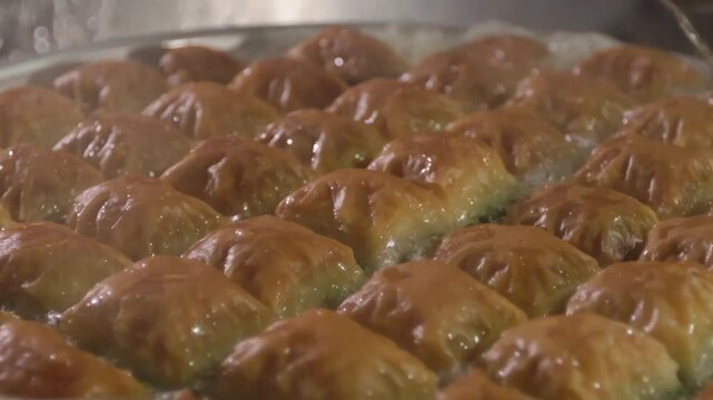 10-bit slow motion close-up of hot sugar syrup being poured onto classic square-cut baklava. Capturing the bubbling sizzle and golden layers of authentic Turkish dessert preparation.