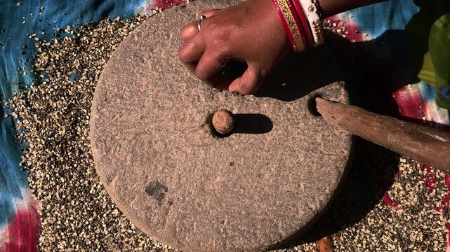 An Indian village woman grinding black gram lentils on a hand-driven stone mill showcases traditional agriculture-based lifestyles, homemade food culture, and timeless rural craftsmanship.