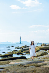 One Chinese woman enjoying the beautiful landscape of beach and ocean and lighthouse at Sanya Dongtian Park (Daxiao Dongtian Scenic Area) in Sanya, Hainan, China
