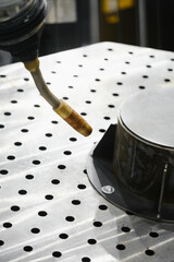 Industrial robot arm with MIG MAG welding torch positioned over perforated fixturing table for gas shielded arc welding of metal parts