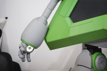 Close-up of green and gray humanoid robot arm with articulated fingers above computer desk in modern tech workspace