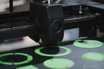 Industrial 3D printer extruder head printing multiple black plastic parts on build plate during additive manufacturing process. Close-up of heated 3D printer nozzle