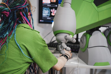 Woman and humanoid robot arm with articulated fingers above computer desk in modern tech workspace, working together, pregaming and operating 