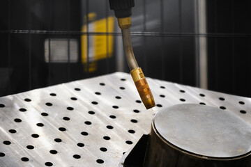 Industrial robot arm with MIG MAG welding torch positioned over perforated fixturing table for gas shielded arc welding of metal parts