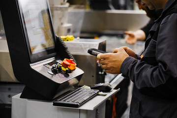 Factory technician using data collection device to log operations on CNC control console with digital display and manual controls
