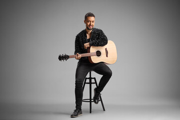 Fototapeta premium Young elegant man sitting on a stool with an acoustic guitar