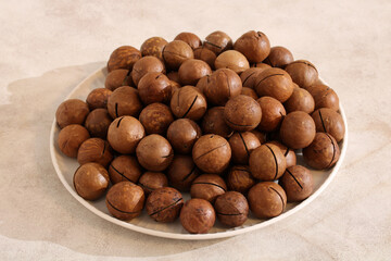 Fototapeta premium Macadamia nuts in shell pile on plate